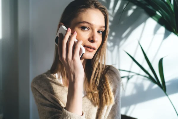 happy young woman sitting and talking on a smartphone, calling a 0300 number in UK
