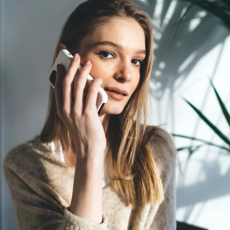 happy young woman sitting and talking on a smartphone, calling a 0300 number in UK