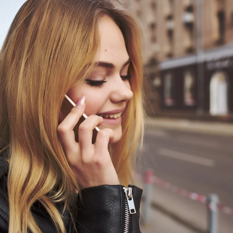 cute blonde in black jacket walking outdoors calling 0300 Number on Virgin Media