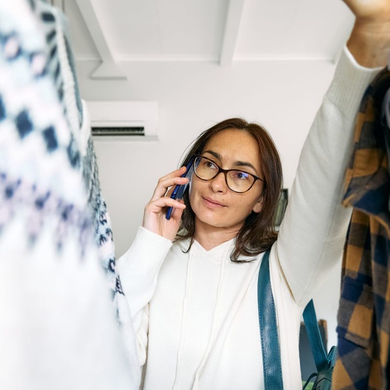 happy woman buying new clothes in store knitted, holding a phone while calling an 0300 number on Sky Talk