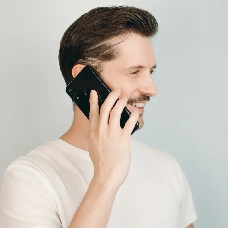 young man smiling and talking on a smartphone dialling a 0300 number